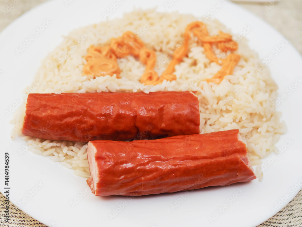 Dinner meal with rice and two sausages and orange color sauce on light color table cloth. Simple tasty food. Dinner meal with rice and two sausages and orange color sauce on light color table cloth. Simple tasty food.