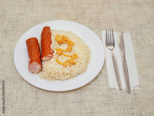 Dinner meal with rice and two sausages and orange color sauce on light color table cloth. Simple tasty food.