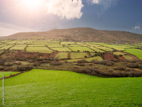 A beautiful landscape with a hillside covered in grass and trees. The sun is shining brightly, creating a warm and inviting atmosphere. Nature scenery in county Kerry, Ireland. Irish farmland.