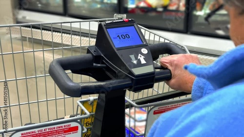 An elderly woman rides a motorized shopping cart through a grocery store, using the electric scooter’s basket to collect items while navigating the aisles.  	