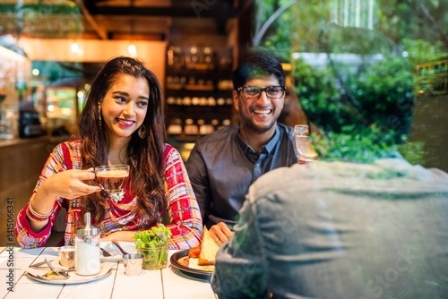 Obraz na płótnie A couple enjoying coffee at a cafe. Smiling and relaxed, they share a moment. The cafe setting is cozy, with warm lighting and a friendly atmosphere. Young Indian friends eating lunch at restaurant. w salonie