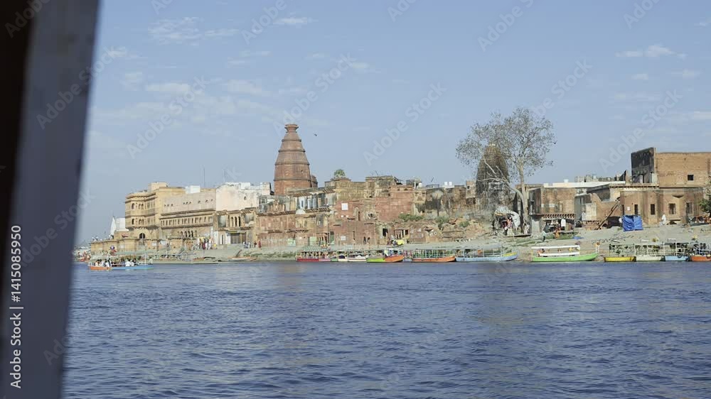 From across the river, a long view of Vrindavan town showcases temples, the town, people, and boats. This perspective highlights the picturesque setting of the area. From across the river, a long view of Vrindavan town showcases temples, the town, people, and boats. This perspective highlights the picturesque setting of the area.