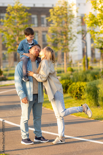 Happy family, activity lifestyle concept. Dad, mom and little boy son spend time together, walking in city park on summer vacation at sunset. Child sits on his father's shoulders. High quality photo