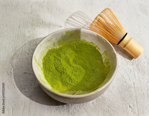 Bowl of matcha powder on light background with bamboo whisk and soft shadows.