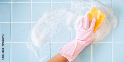 Tableau sur toile A hand in a pink glove scrubs a blue tiled surface with a yellow sponge, creating soapy bubbles