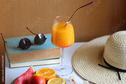 Glass of cocktail, straw hat, sunglasses, books, fresh fruit, chocolate and accessories. Summer essentials on the table. Selective focus.