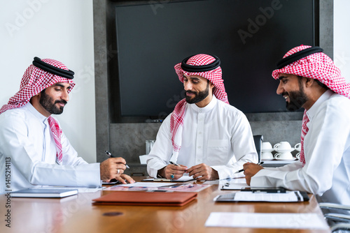 Arab businessmen wearing emirati and saudi kandura meeting in office for business deal - Corporate business group of middle-eastern people working in an international company in middle east