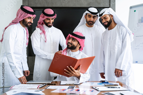 Arab businessmen wearing emirati and saudi kandura meeting in office for business deal - Corporate business group of middle-eastern people working in an international company in middle east