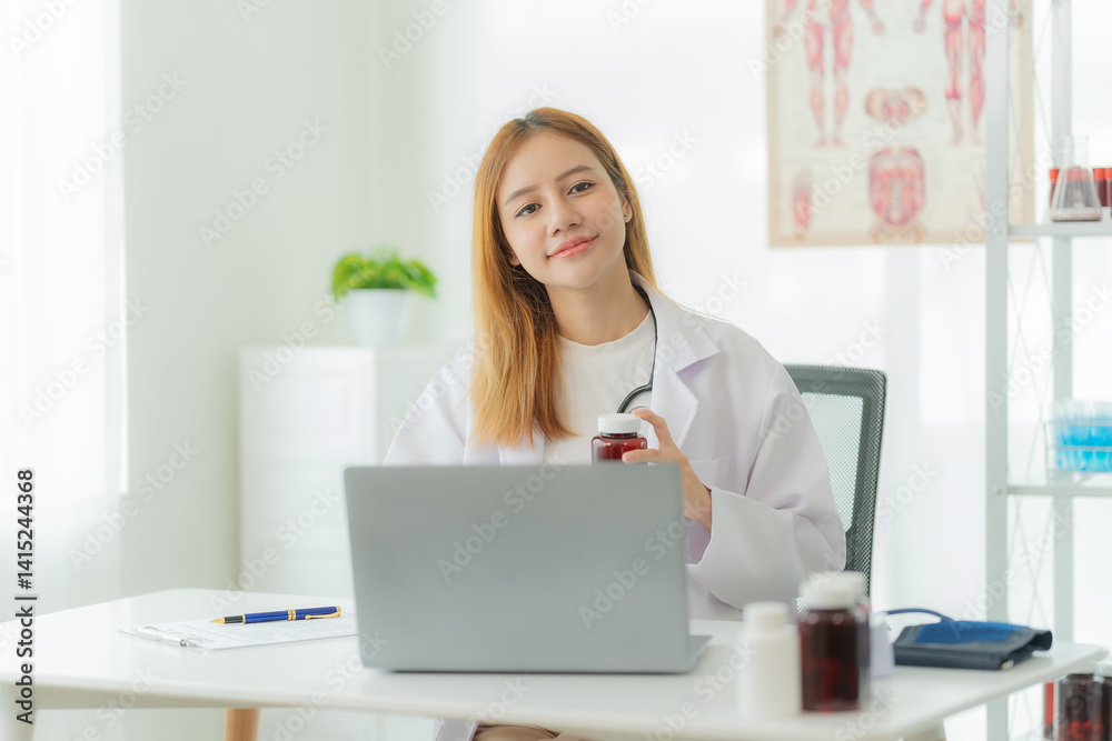 Smiling Asian female doctor in lab coat and stethoscope sitting next to online consultation table in doctor's office Smiling Asian female doctor in lab coat and stethoscope sitting next to online consultation table in doctor's office