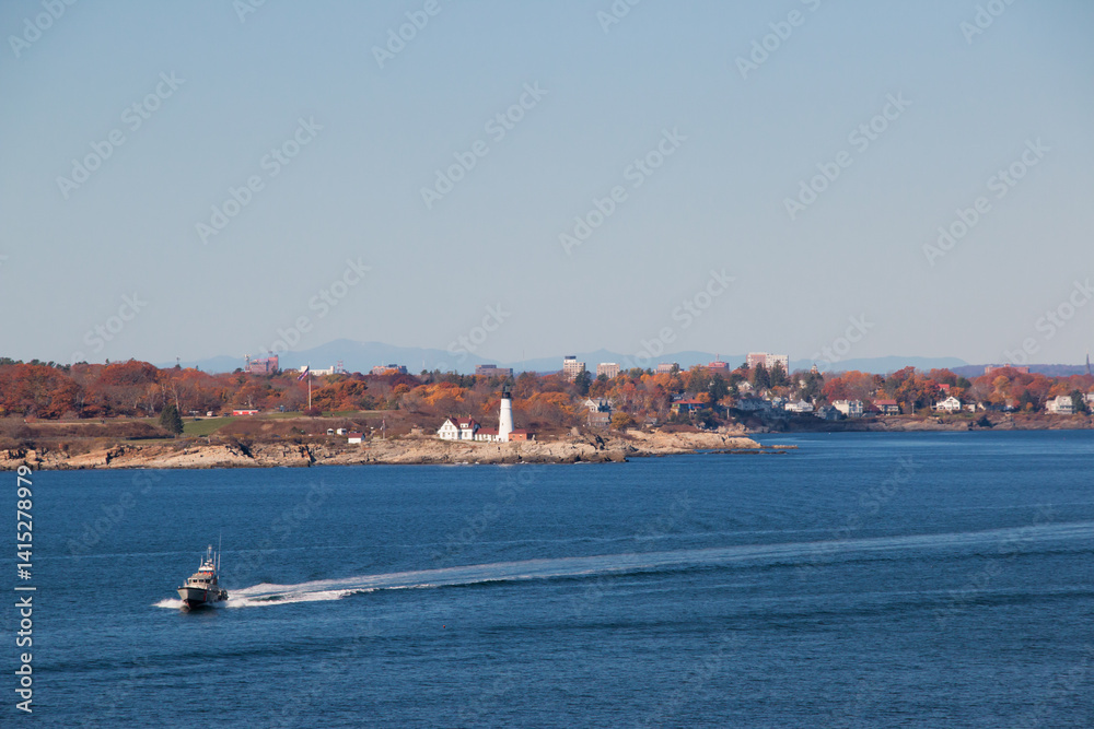 Obraz premium Portland Head Light in Cape Elizabeth, Maine as seen from the Atlantic Ocean on an autumn morning and a coast guard boat passing. An historic 1791 lighthouse still in operation.