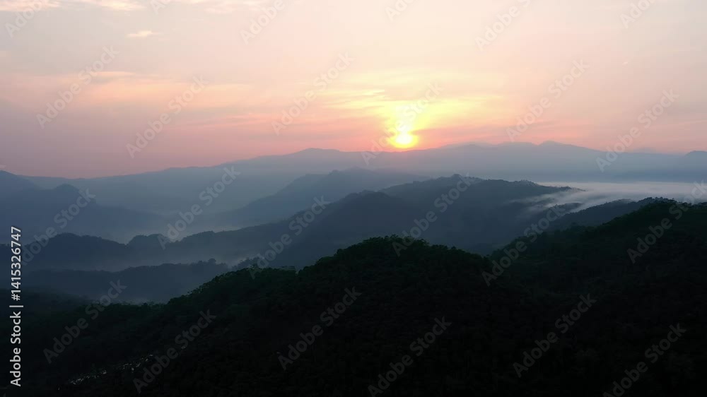 Aerial view of sunrise behind rolling hills in Kasepuhan Pasir Eurih, Banten, Indonesia, with soft golden light illuminating the natural landscape. Aerial view of sunrise behind rolling hills in Kasepuhan Pasir Eurih, Banten, Indonesia, with soft golden light illuminating the natural landscape.