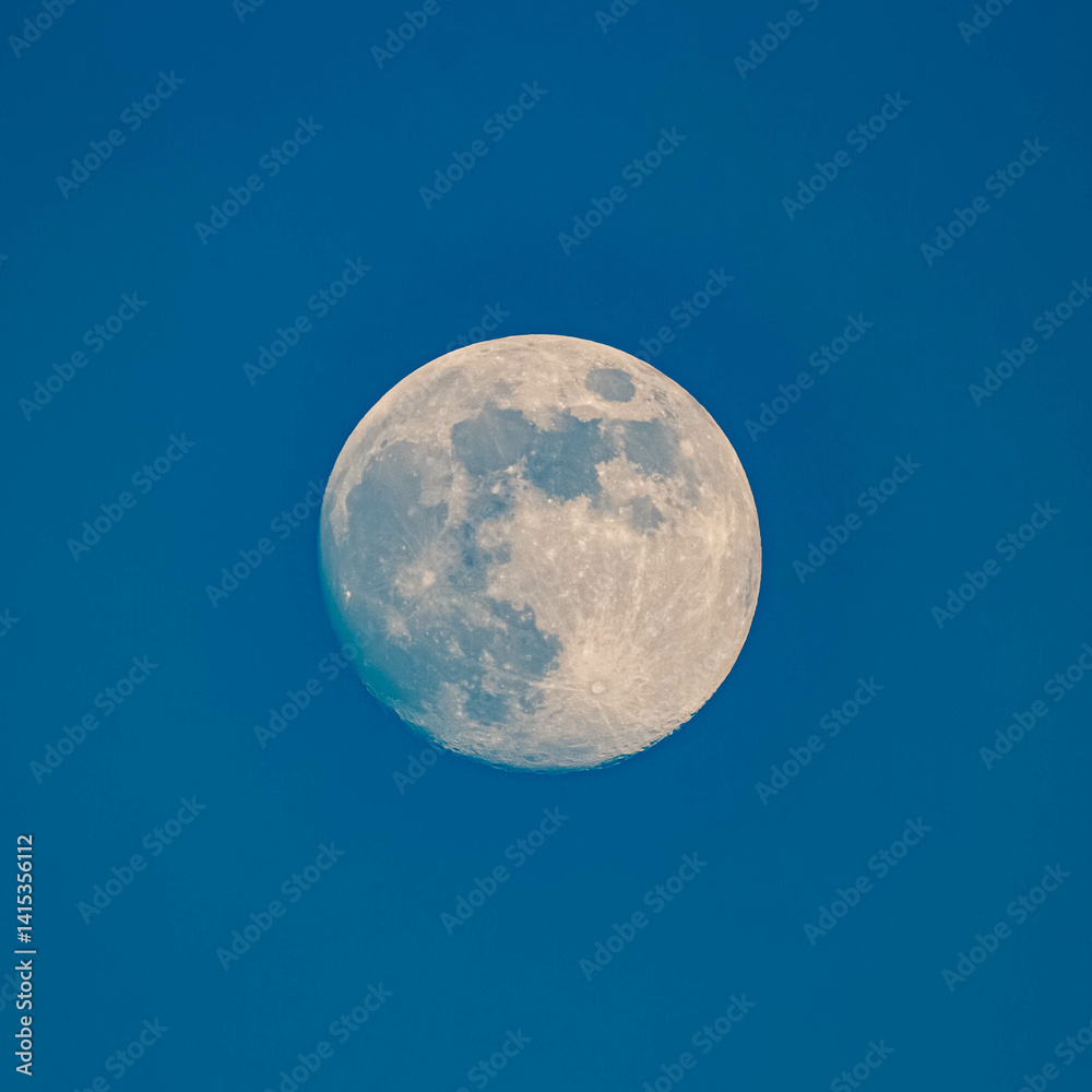 Detailed megazoom (600mm) winter view of the moon with craters during daytime with blue sky