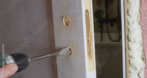 The carpenter uses a drill bit to make a hole for the lock in the door.