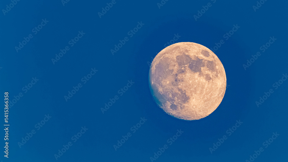 Detailed megazoom (600mm) winter view of the moon with craters during daytime with blue sky