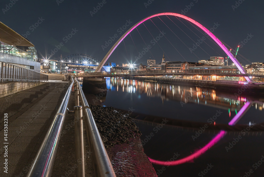 Nightscape view of The Iconic gateshead millennium bridge with Tyne bridge and dark sky in the background. The pedestrian bridge spanning the River tyne with reflection in river, Space for text.