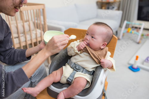 Obraz na płótnie Parent feeding baby sitting on high chair w salonie