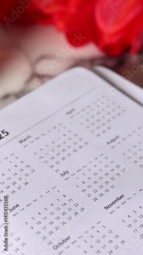 2025 new year notebook planner with annual calendar on white marble table with cup of coffee and red tulips. Vertical video. Close-up.