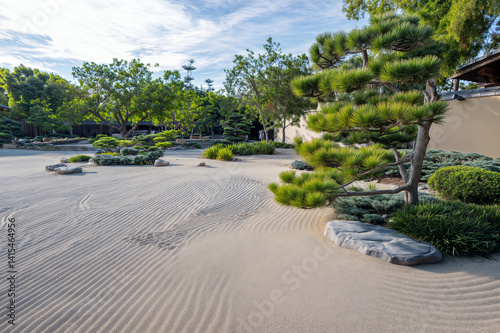 Obraz na płótnie The image depicts a serene Japanese garden with raked sand, various shrubs, and a low stone wall w salonie