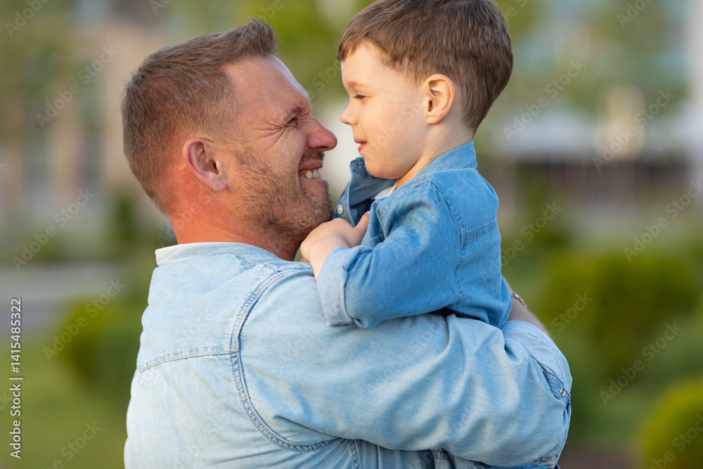 Funny and emotional image. Side view father holding his son in his arms while walking in city park on summer. Celebrating happy Father's Day. High quality photo