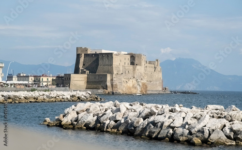 Ancient Castel dell'Ovo fortress overlooking Bay of Naples with Mount Vesuvius in background. Historic seaside landmark captures Mediterranean coastal charm and Italian architectural heritage.
