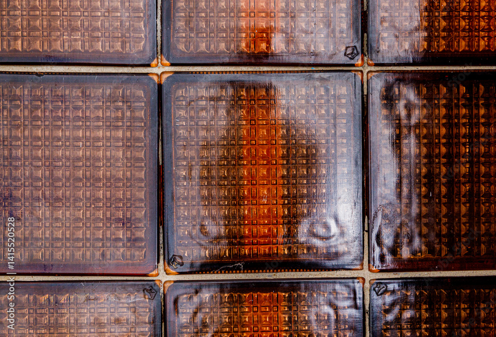 Exploring intricate textures of warm-toned glass tiles with deep shadows and reflections under soft light
