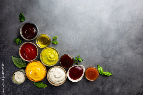 Set of different bowls of various dip sauces, on dark background, top view photo