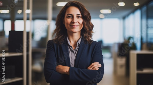 Confident female entrepreneur standing with arms crossed, wearing a techie suit, exuding leadership in a corporate setting.

