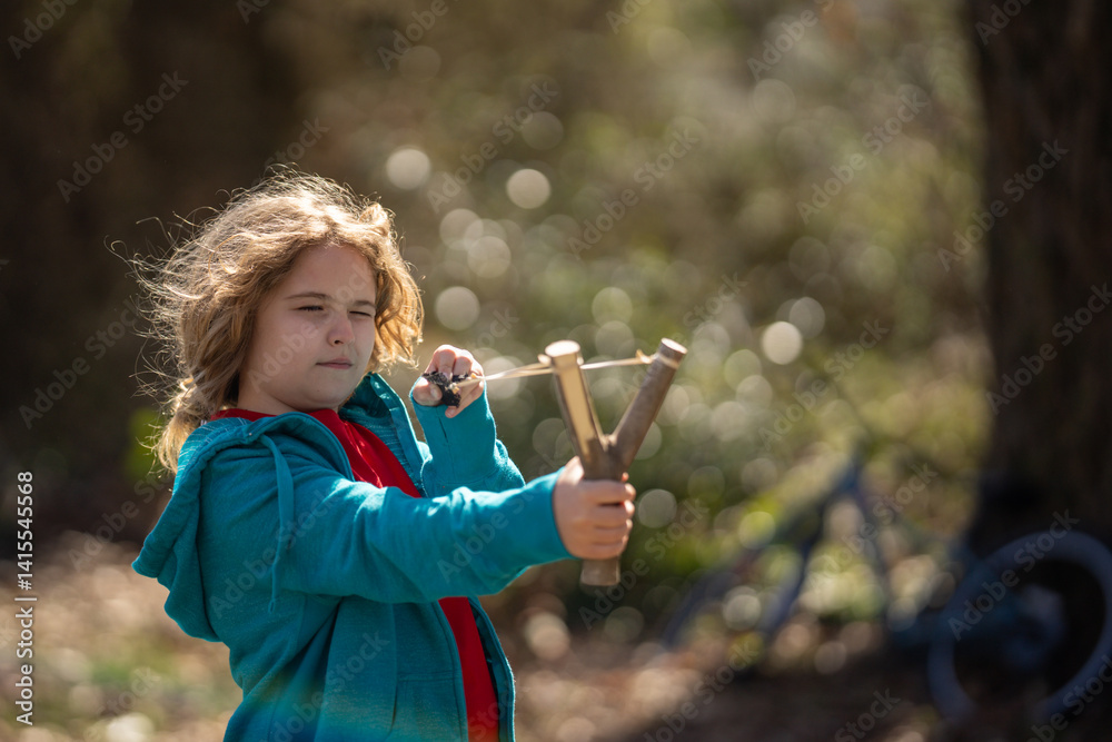 Slingshot in kids hand. Child holding catapult. Boy aiming with sling. Child playing with slingshot. Handmade wooden slingshot. Child aiming at target. Child with slingshot. Outdoor fun with catapult.
