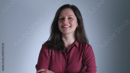 A woman in a red shirt stands confidently with her arms crossed, exuding self-assurance and poise.