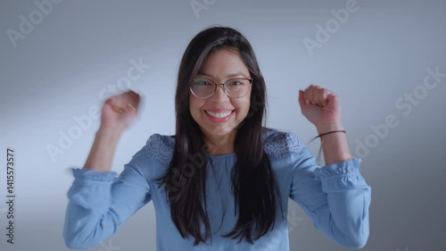Woman in glasses and blue shirt, smiling and extending hands, exudes warmth and approachability.