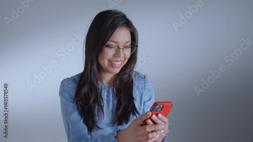 Woman with glasses and blue shirt smiles, holding red phone, exuding joy and engagement.