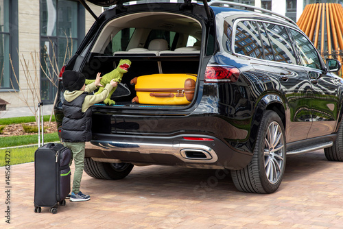 Obraz na płótnie A little boy stands near a car with a suitcase and is going on a road trip. Family road trip. Happy child with suitcases and toys going on journey. High quality photo w salonie