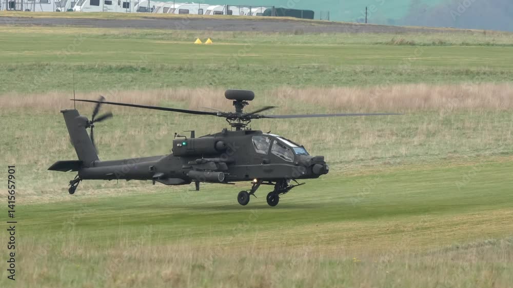 British army AH-64E Boeing Apache Attack helicopter gunship in flight and hovering close to a grass runway British army AH-64E Boeing Apache Attack helicopter gunship in flight and hovering close to a grass runway