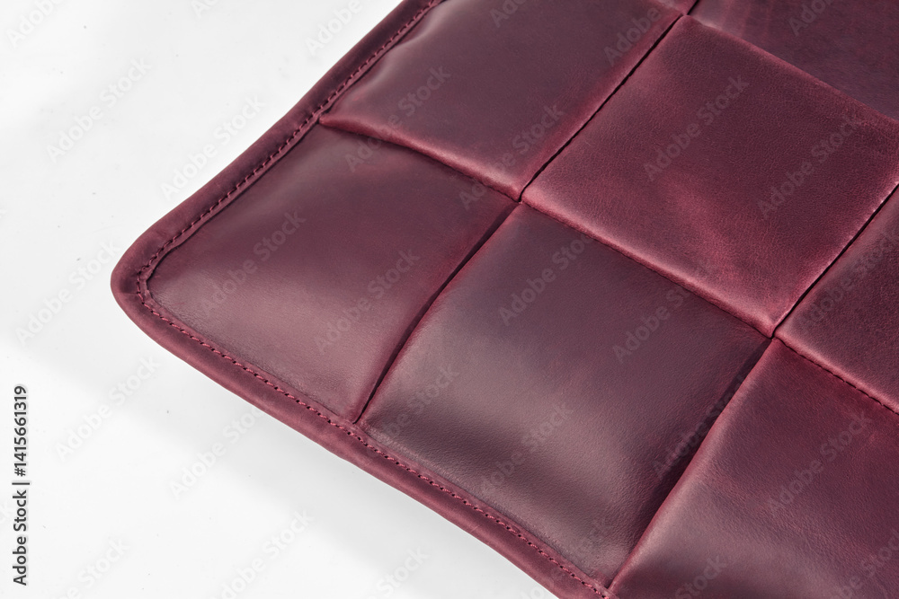Close-up of corner of padded burgundy leather cushion showing stitching