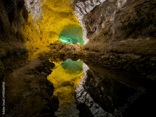 Obraz na płótnie The Cueva de Los Verdes cave in colorful light with reflection on water in Lanzarote, Spain This cave a part of the volcanic tube generated after the eruption of the La Corona Volcano w salonie