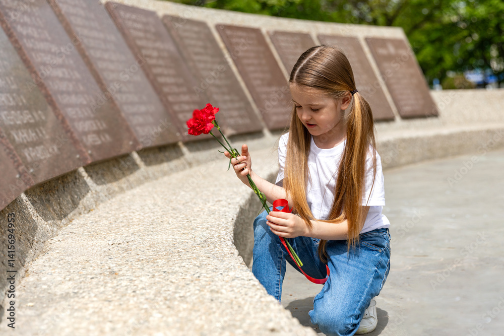 The memory of soldiers in Great Patriotic War. Little girl laying red carnations at the monument to fallen soldiers in world War II. Victory Day on May 9.