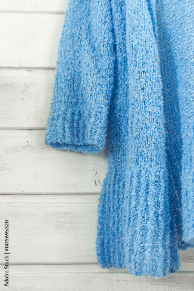 Blue cotton knitted cardigan on white wooden background. Soft blue knitted sweater on hanger in sunlight. Knitting pattern background. Summer knitted fashion. Cozy hobby. Craft product concept.