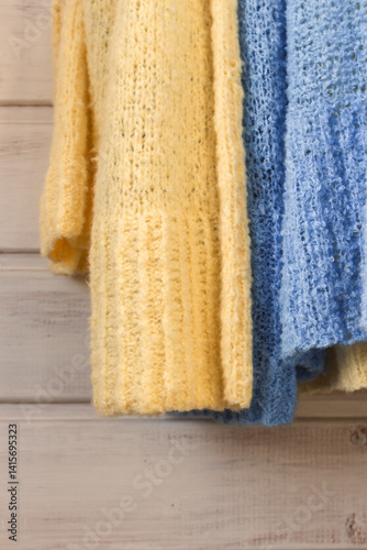 Obraz na płótnie Blue and yellow cotton knitted cardigan on white wooden background. Soft knitted sweaters on hanger in sunlight. Summer knitted fashion. Cozy hobby. Craft product concept. Ukrainian fashion. w salonie