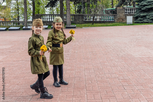 Obraz na płótnie Patriotic education of youth. Little girls in an old Soviet military uniform laying flowers at the eternal flame near the monument to fallen soldiers in world War II. Victory Day on May 9. Copy space w salonie
