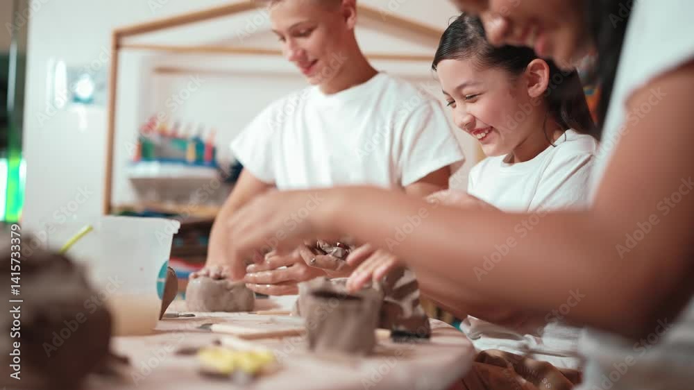 Handsome student dipping hand in to water to soften clay at art classroom. Group of diverse children working or modeling vase. Happy boy put water to young girl while laugh with happy. Edification Handsome student dipping hand in to water to soften clay at art classroom. Group of diverse children working or modeling vase. Happy boy put water to young girl while laugh with happy. Edification