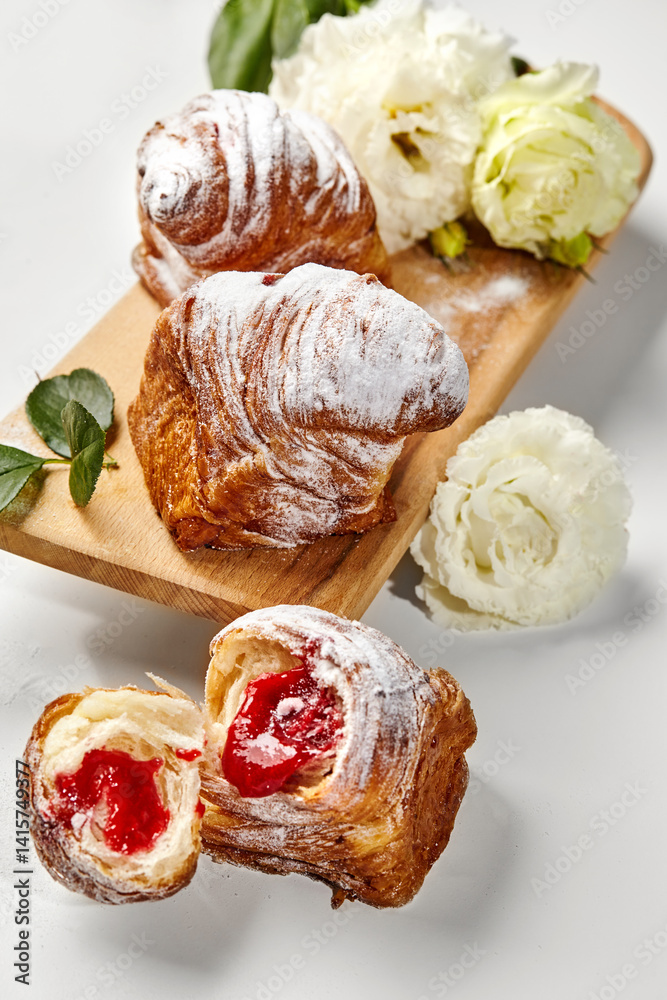 Delicious puff pastry cruffins with strawberry filling and icing sugar on wooden board