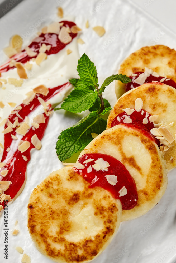 Syrniki with raspberry jam, almond flakes, sour cream and mint on white plate