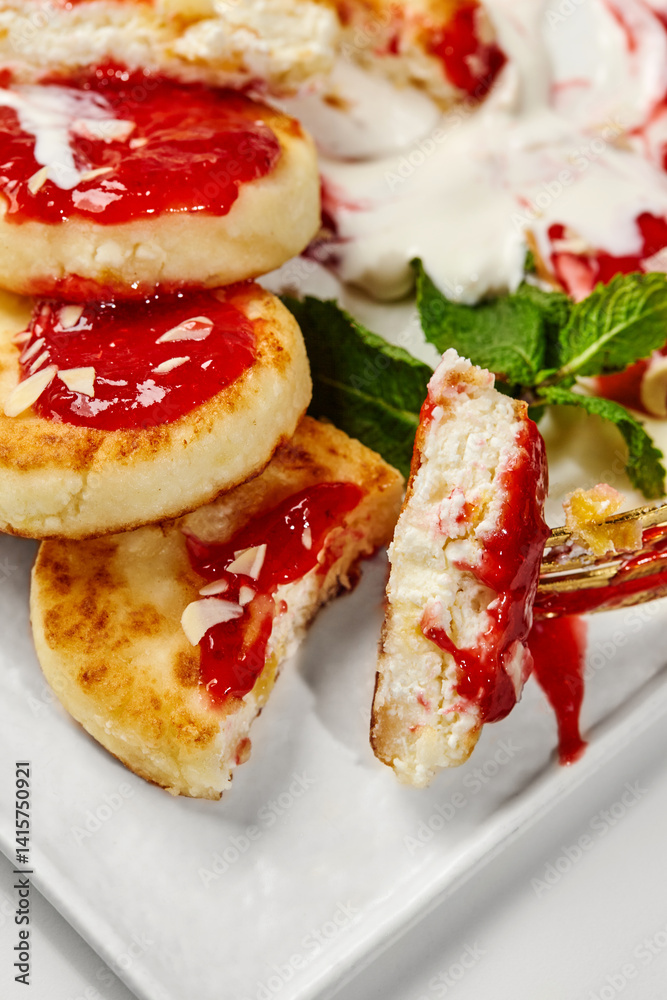 Syrniki with strawberry jam, sour cream and mint being eaten with a fork