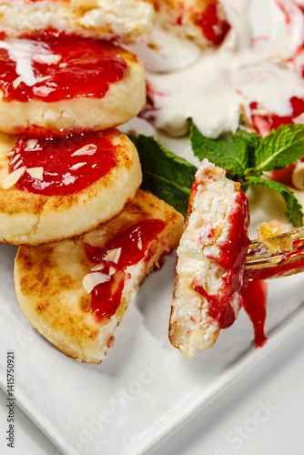 Syrniki with strawberry jam, sour cream and mint being eaten with a fork