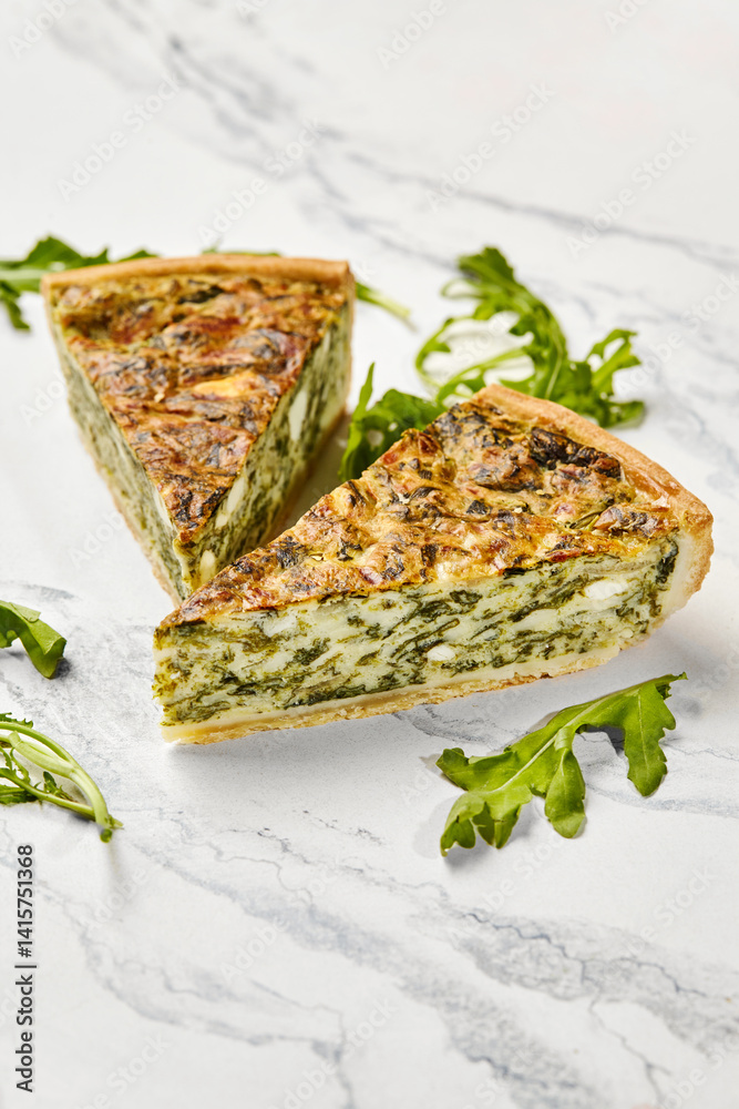 Delicious spinach and feta quiche slices with fresh arugula on marble