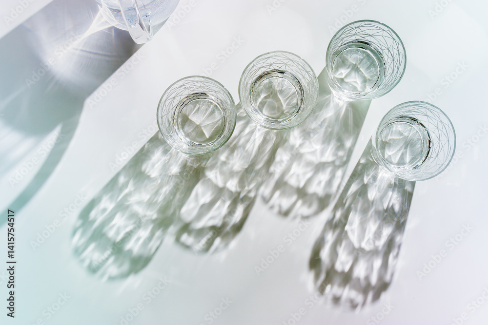 Water Glasses and water jug with Shadows and sunlight Reflection on white background, colored photo minimal style, aesthetic summer still life, refraction throug crystal shine cups, caustics
