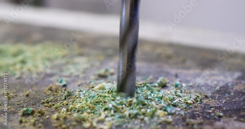 A precision metal drill bit penetrates the chipboard, producing fine dust and debris, creating complex holes during the furniture manufacturing process.
