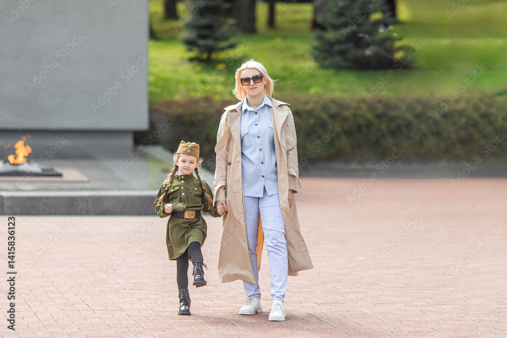 Patriotic education of children. Mother with little girl on Victory Day. Girl in a military uniform, military cap near the memorial. Photo for the May 9 celebrations