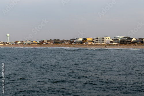 Distant view of oceanfront homes line the shore at Oak Island, North Carolina, with gentle Atlantic waves in the foreground under soft, hazy daylight