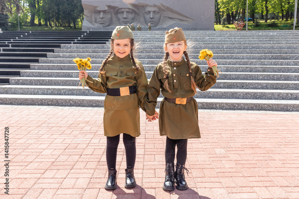 Patriotic education of children. Little girls in a military uniform, military cap, hold flowers in hands against the background of the memorial. Victory Day on May 9